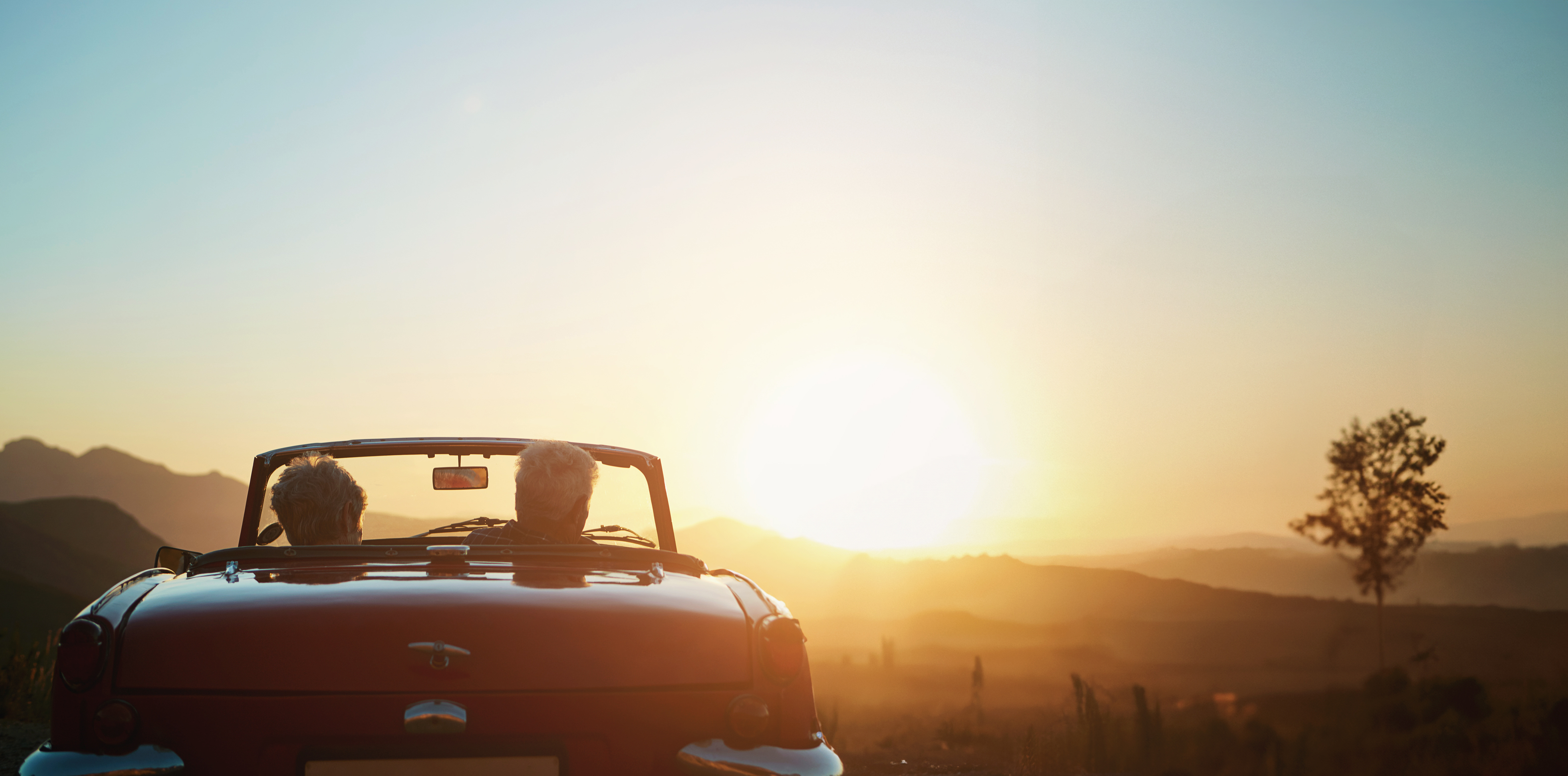 Älteres Paar im roten Cabrio blickt in den Sonnenuntergang über den Hügeln