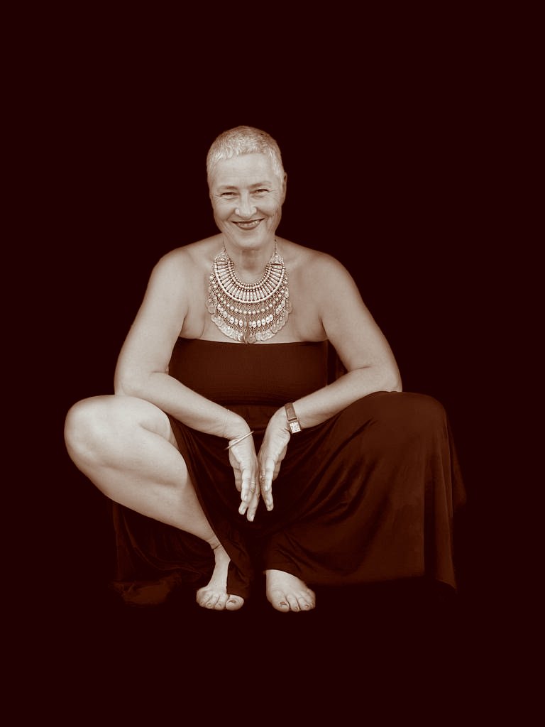 Andrea Lindau sitzt in der Hocke, lächelnd, mit Halsschmuck, vor schwarzem Hintergrund